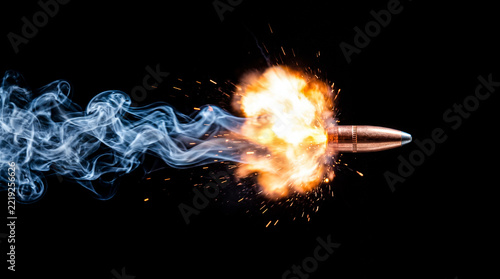 Close-up shot of a bullet in motion emitting a bright fiery explosion and a wispy blue smoke trail against a stark black background