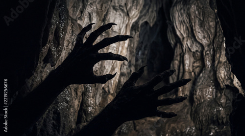 Black silhouette of scary monster hands with long sharp claws reaching forward from a dark cave for horror and Halloween themes