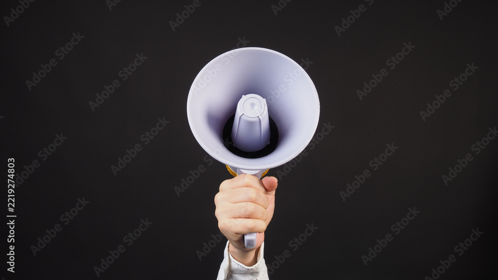 Fototapeta premium Hand holding a white megaphone against a dark background