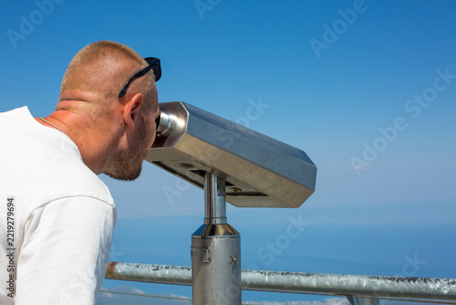A man looks through binoculars from a mountain peak, taking in the breathtaking view of the sea. Tourism concept.