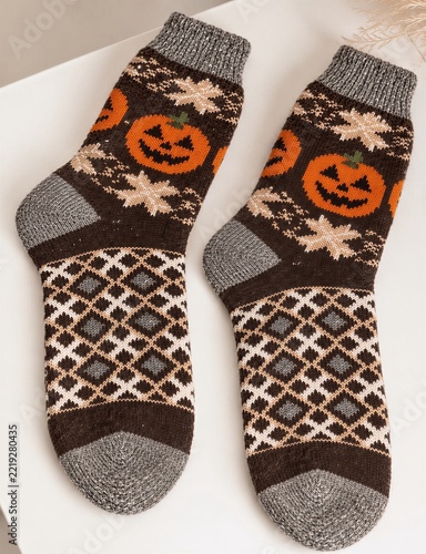 Cozy knitted Halloween socks with jack-o-lantern pumpkin patterns, warm autumn fashion accessories, festive seasonal clothing, geometric ornaments and soft wool texture on a white background
