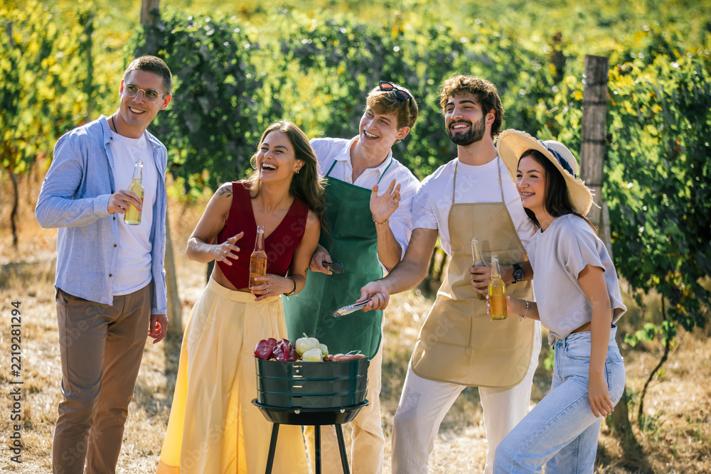Naklejka premium Cheerful friends gathering around food and drinks in a vineyard