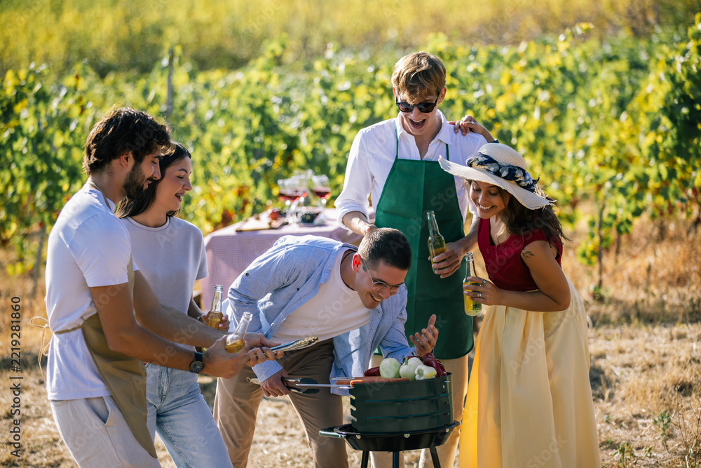 Fototapeta premium Friends preparing a meal together around a barbecue in the vineyard