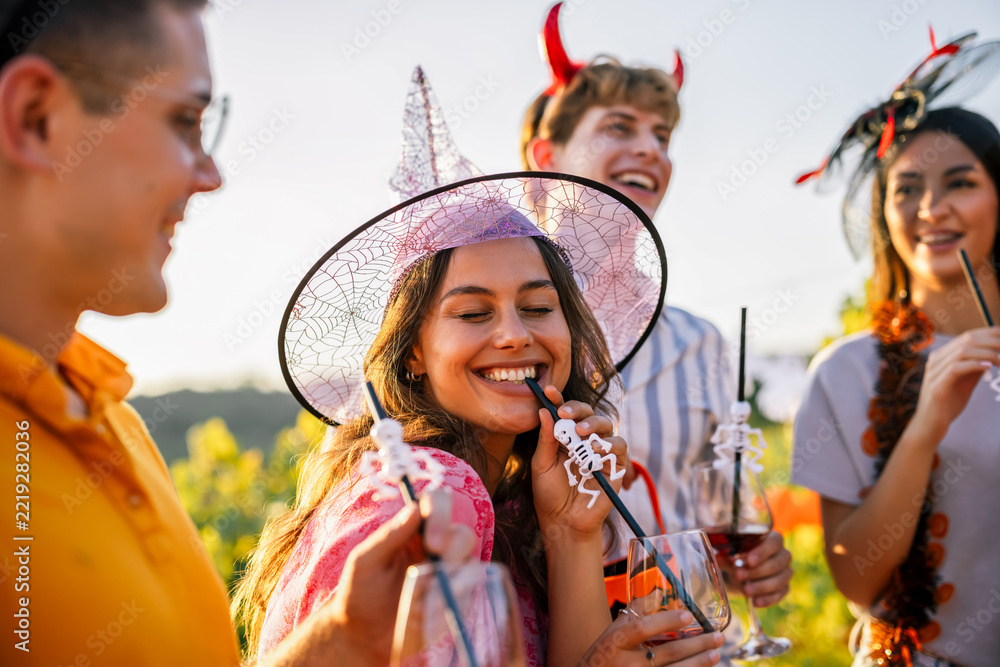 Fototapeta premium Woman in witch hat smiling with friends at a Halloween vineyard party