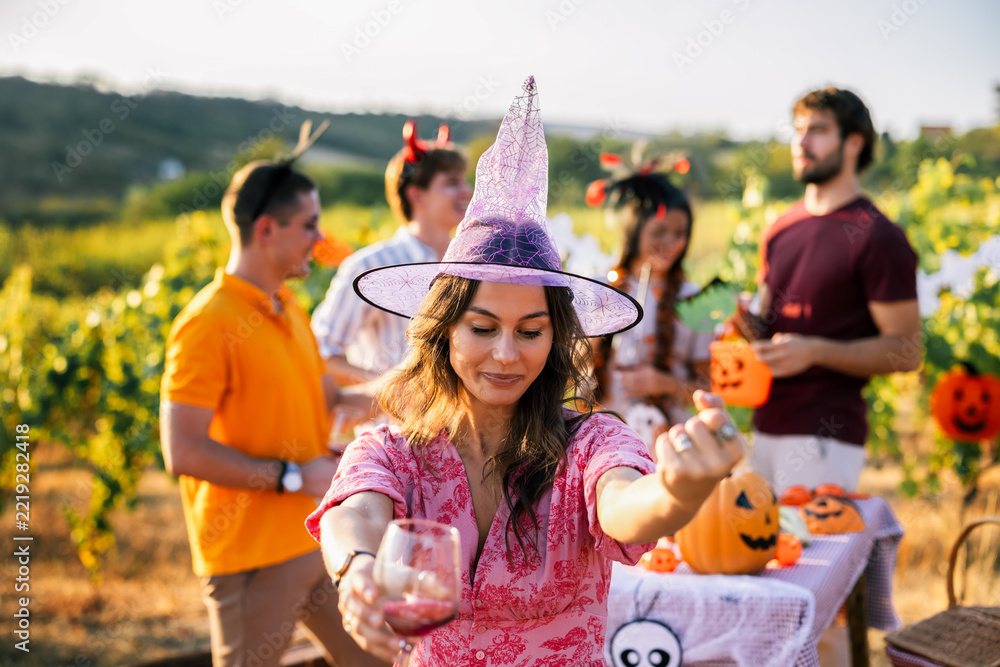 Fototapeta premium Woman in witch costume holding a drink during a Halloween vineyard celebration
