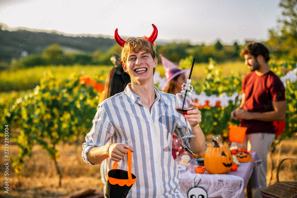 Naklejka premium Man in devil horn costume smiling with a wine glass at a vineyard party