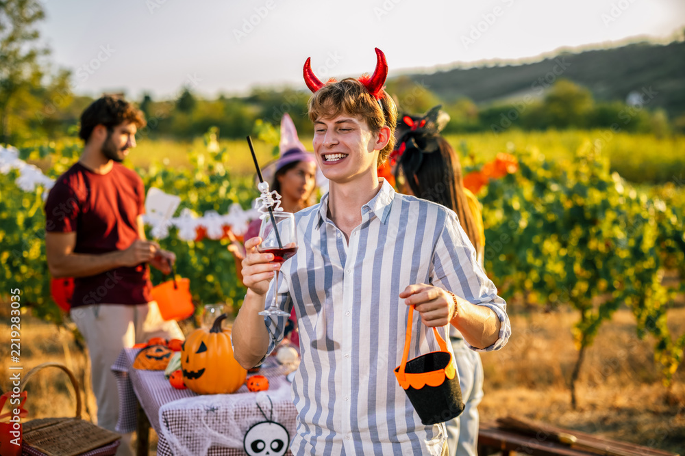 Fototapeta premium Man wearing devil horns holding a wine glass during an outdoor Halloween party