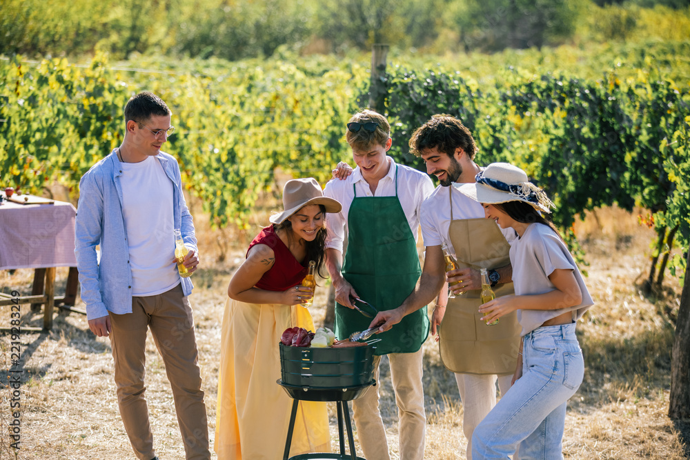 Fototapeta premium Friends gathering around an outdoor grill while preparing food in a vineyard