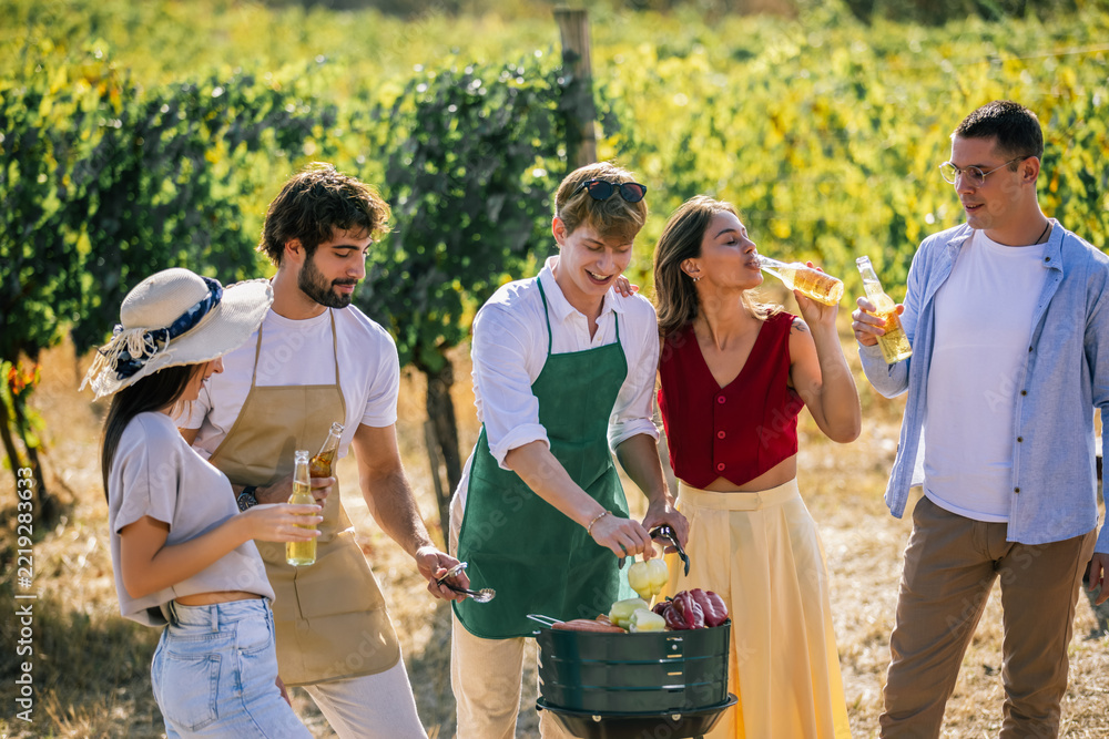 Fototapeta premium Friends preparing food and enjoying drinks together in the vineyard