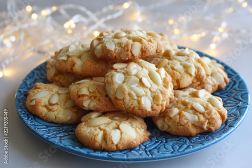 Italian pignoli cookies (pine nut cookies) on a blue plate before plain ivory background with white christmas lights