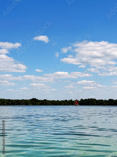 A view on a Dnipro river with a small yacht with red sail on a bright summer day