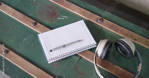 Camera is panning right and down, revealing notebook, pen, headphones on worn bench to show texture