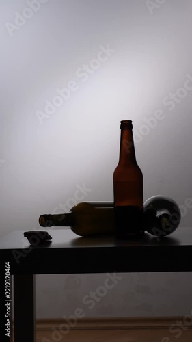 Vertical video silhouetted hand opening a beer bottle on a table with other alcohol bottles, illustrating concepts of alcohol abuse, addiction, and mental health struggles in a dark, suggestive settin