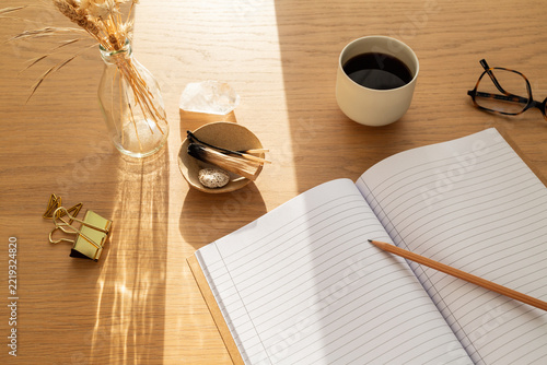 Bureau en bois ensoleillé avec cahier ouvert, tasse de café, fleurs séchées et palo santo
