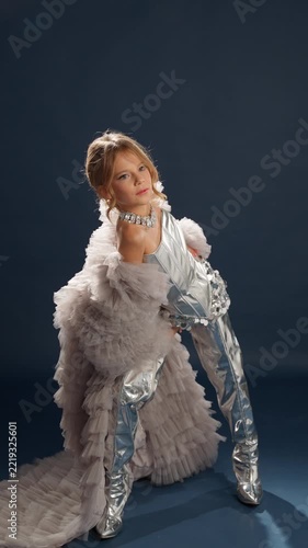A girl in a silver outfit poses in the studio. Children's fashion concept.