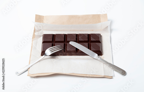 Obraz na plátně Fork and knife resting on a large dark chocolate bar