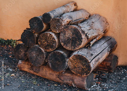 Stacked Firewood Logs with Cracked Cut Ends and Weathered Bark Against a Rustic Orange Wall