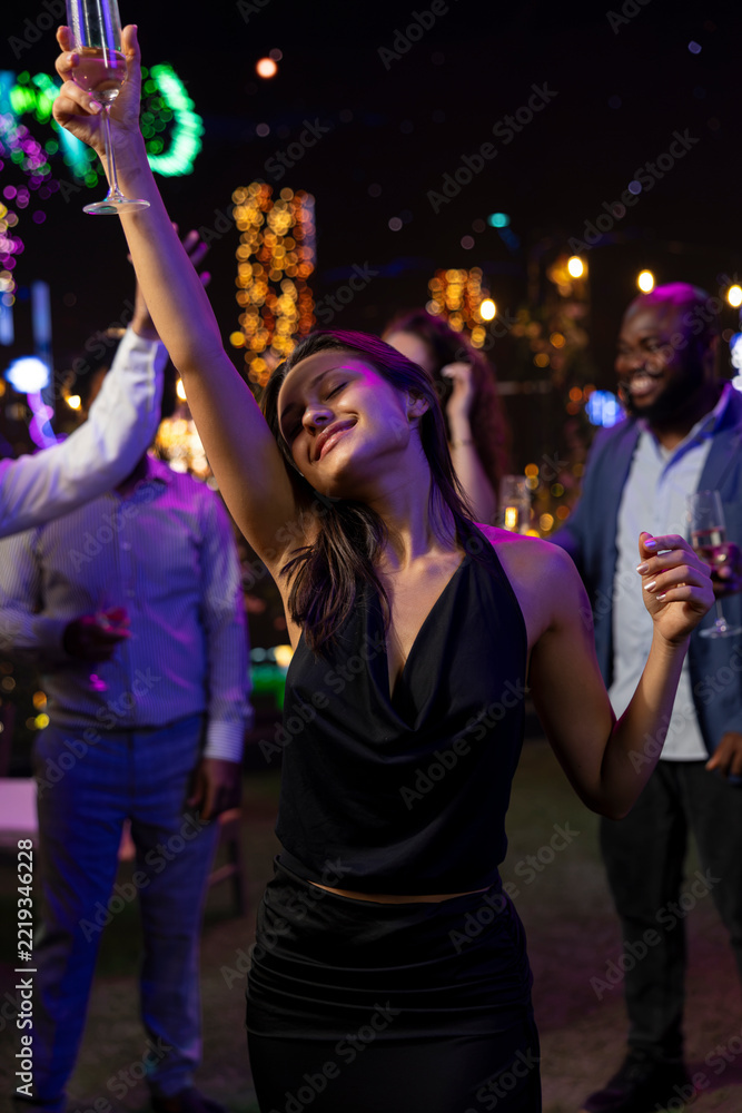Fototapeta premium Smiling woman dances ecstatically at a New Year's Eve party, feeling emotional as she listens to music and celebrates midnight at the festive rooftop event.
