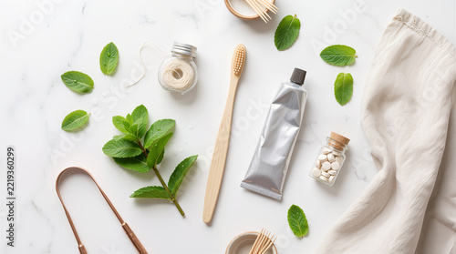Eco-friendly zero waste oral care set with bamboo toothbrush, natural toothpaste, chewable tablets, dental floss, tongue scraper, and fresh mint on marble