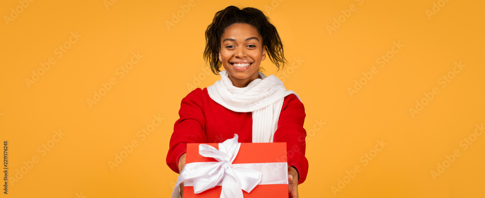 Fototapeta premium Happy Smiling Young African American Woman Holding Red Gift Box With White Bow, Displaying Excitement And Joy At Studio Setting. Gift Giving And Celebration Concept.