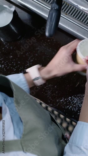 Vertical video: With hung portafilter barista in apron fixing head, wiping grind and checking time