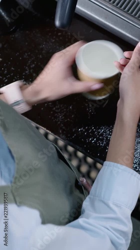 Vertical video: Leaning barista in blue top olive apron fitting portafilter into group for espresso