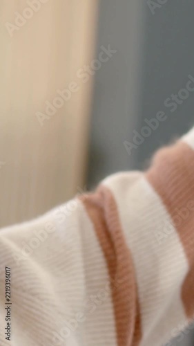 Vertical video: Lifting sleeve, man in striped sweater moving in lounge, addressing smartphone lens