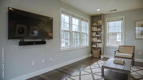 Modern living room interior with a television mounted on the wall, a cozy sofa, a wooden coffee table, and a bookshelf filled with white books in a bright setting