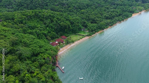 Aerial footage captures the vivid green rainforest of Ilha Grande meeting tranquil turquoise waters along an unspoiled sandy coastline, under even daylight.