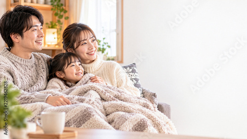 冬のリビングで毛布にくるまり笑顔でくつろぐ日本人の親子3人、暖かい家庭で過ごす幸せな家族団らんと余白のある風景