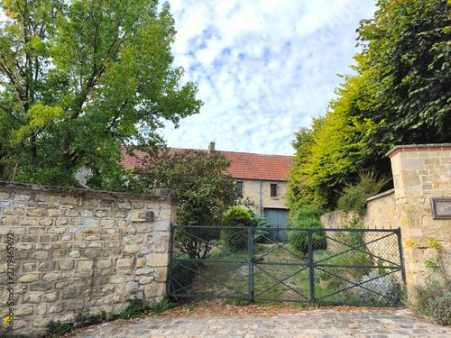 Fotografie Old Iron Gate and Stone Wall Leading to Rustic French Farmhouse with Red Tile Ro