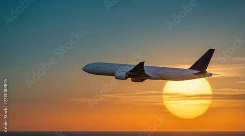 A commercial airplane flying through the bright orange sunset sky.