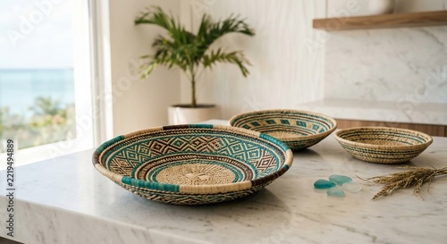 Woven decorative baskets featuring geometric turquoise patterns arranged on a bright marble countertop inside a modern room with tropical plant decor near a sunlit window
