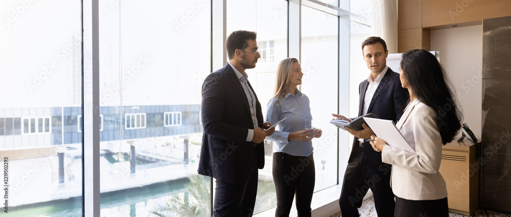 Fototapeta premium Group of multiethnic professionals standing in office, discussing business strategy, engaging in collaboration, project planning, banner. Corporate partnership, informal team meeting, teamwork concept