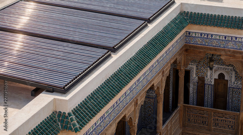 Solar thermal collectors and evacuated tubes covering the roof of a traditional Moroccan riad featuring intricate tilework and carved wooden architecture