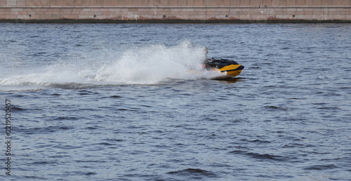 Obraz na plátně A yellow jet ski is speeding along the river at high speed, spraying water, alon