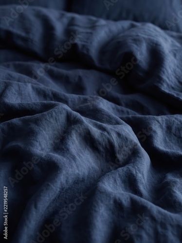 Close-up of rumpled navy blue fabric with soft folds and visible woven texture. Textile background for bedding and home goods. Abstract material surface. Copy space for design