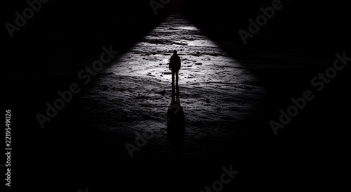 Solitary Figure Walking on a Dark, Textured Path with a Single Spotlight.
