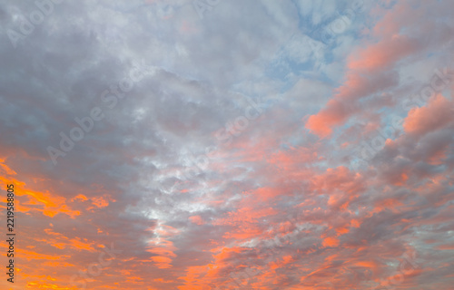 Orange sunset colors illuminate broad gray clouds across expansive evening sky. Textured cloud cover forms dramatic atmospheric backdrop, with warm light glowing near horizon beneath textured cloud