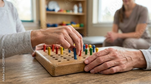 hand dexterity therapy activity closeup Elderly person playing peg solitaire game on wooden table with a caregiver nearby.
