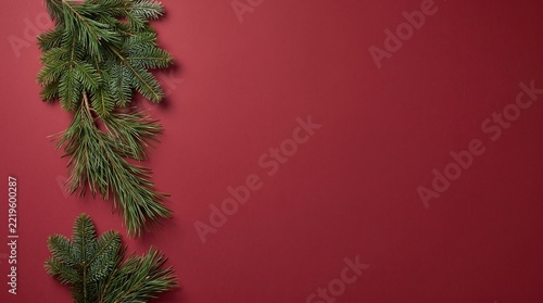 Fresh evergreen pine branches arranged on a textured dark red surface background