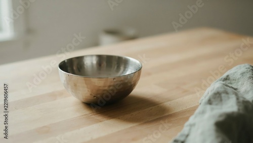 Empty stainless steel pet bowl on a wooden tabletop with a linen cloth