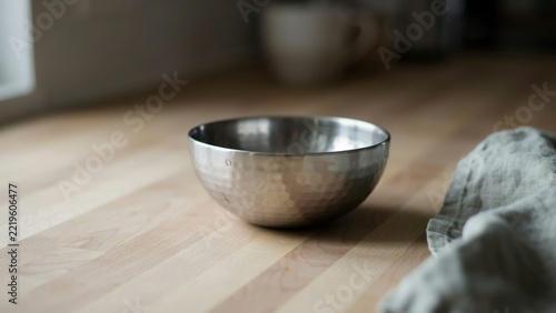 Empty stainless steel pet bowl on a wooden tabletop with a linen cloth