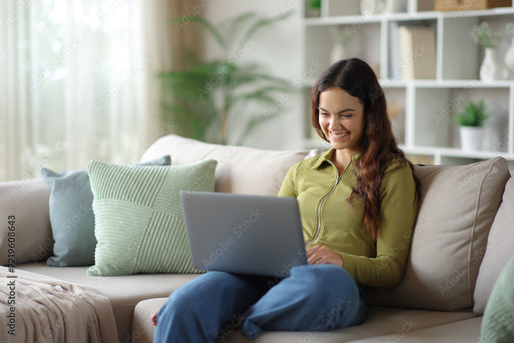 Naklejka premium Happy young woman in green using laptop sitting on a sofa