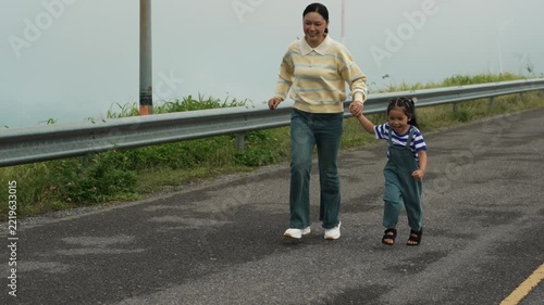 slow motion of mother and preschool child girl holding hand and running on a road on mountain in the morning