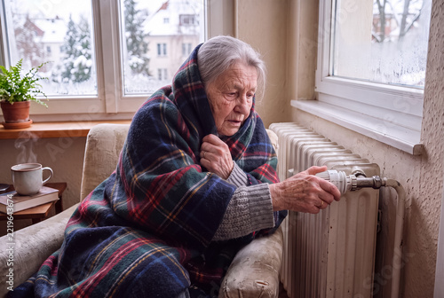 Senior woman feeling cold adjusting radiator temperature during winter