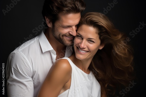 Happy adult couple embracing, showing strong connection and sincere joy on their faces, smiling broadly together, celebrating love, romance, and enduring companionship against a dark background