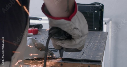 Close up of worker hands in white gloves holding angle grinder on workbench