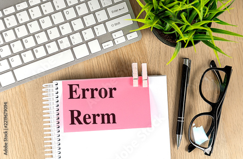 Misspelled text reading error rerm on pink paper clipped to a notebook, with keyboard, pen and glasses on a wooden desk