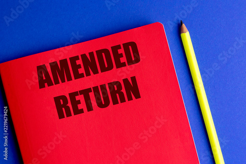 Amended return text on a red notebook beside a yellow pencil on a blue background, tax correction and financial reporting concept